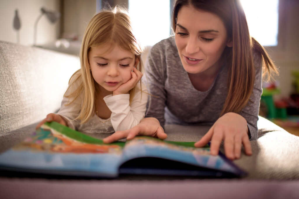 Single mother having fun at home reading with her baby daughter.